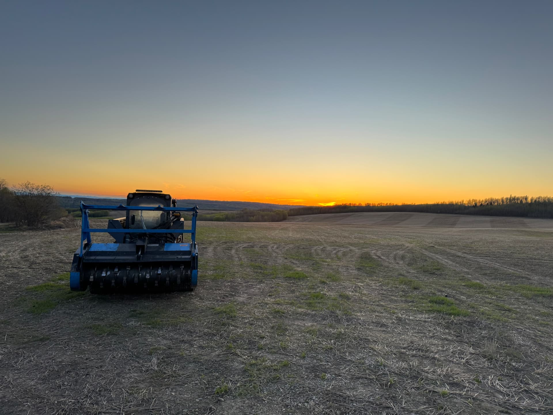 Machine silhouetted against a sunset over a field