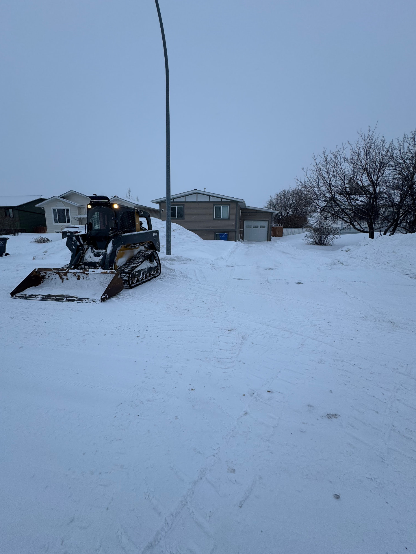 Tracked skid steer clearing snow from a residential driveway